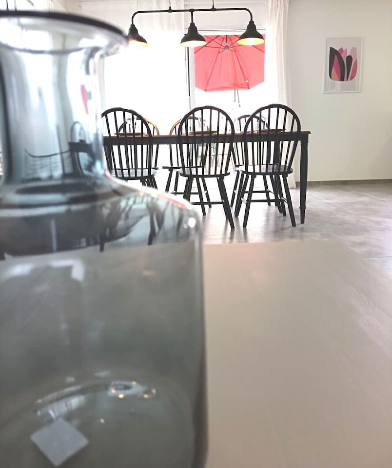 Un comedor con una mesa y sillas, un jarrón de cristal grande y un paraguas rojo.