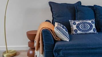 A room with a blue sofa, a patterned throw blanket, and a decorative pillow. A floor lamp with a gold base is positioned to the left.