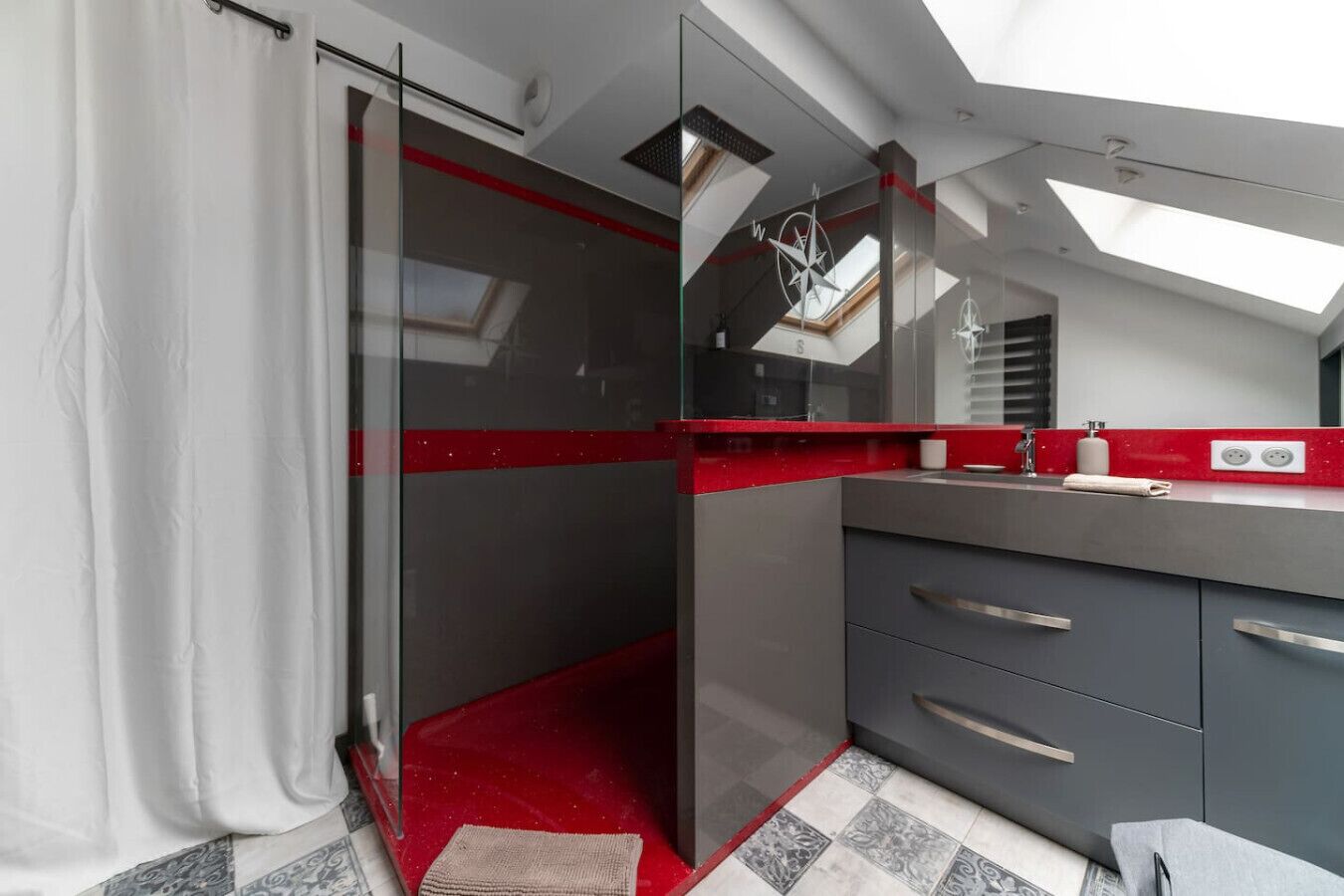 Un baño moderno con cabina de ducha de vidrio, una pared de acento roja y un tragaluz sobre la zona del lavamanos.