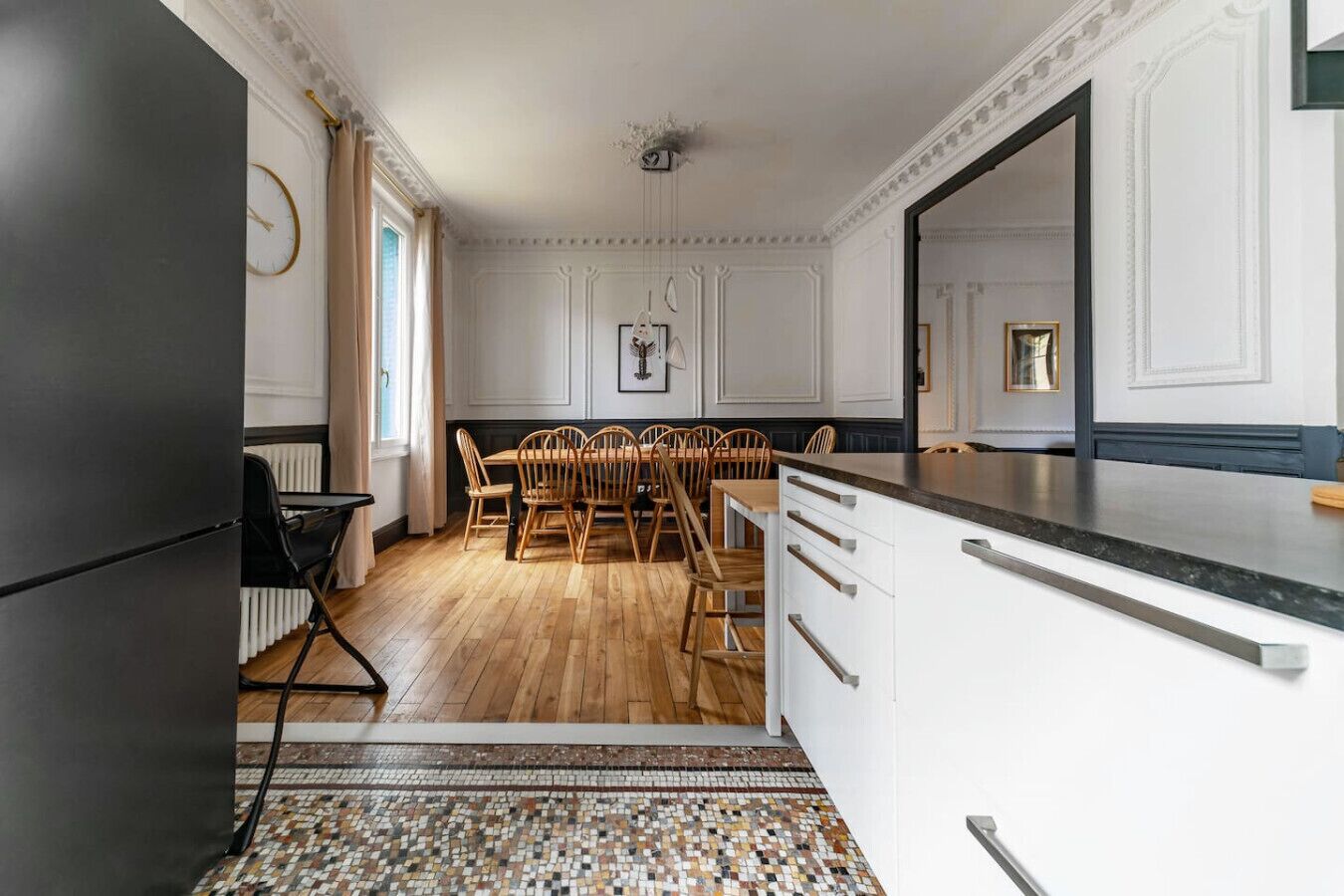 Eine moderne Küche mit weißen Schränken, einem Holzespeisetisch mit Stühlen und einem schwarzen Kühlschrank.