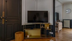 Un salon doté d’un grand téléviseur à écran plat, d’un parquet, d’un pouf rond et d’un tapis à motifs.
