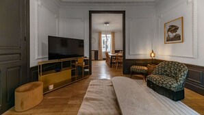Un salon avec un téléviseur, un fauteuil à motifs et un coin repas à l’arrière-plan.