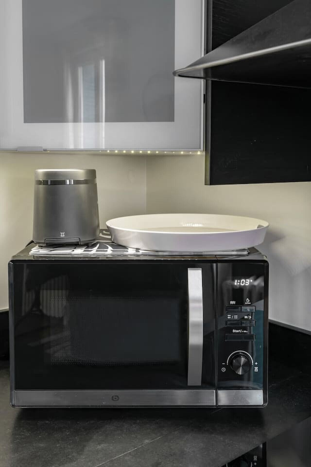 A modern kitchen with a black microwave oven, a coffee maker, and a white electric kettle on top.