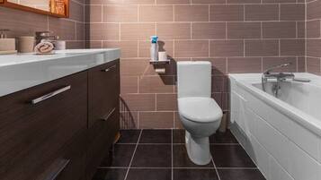 Un bagno moderno con piastrelle scure, un water bianco, una vasca da bagno e mobili in legno.