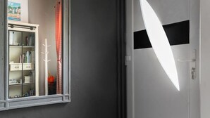 Un pasillo con una pared oscura, una puerta blanca con una franja negra y un ventanal de marco blanco.