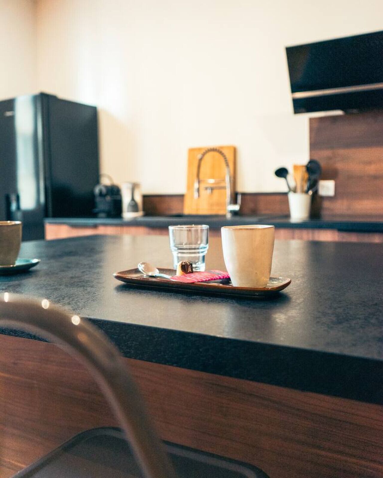 Eine Küchenarbeitsplatte mit einer Schale, die ein Glas und eine Tasse enthält, ein Holzschneidebrett und ein Messer.