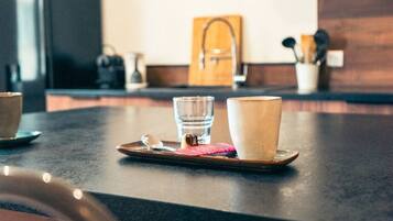 Eine Küchenarbeitsplatte mit einer Schale, die ein Glas und eine Tasse enthält, ein Holzschneidebrett und ein Messer.