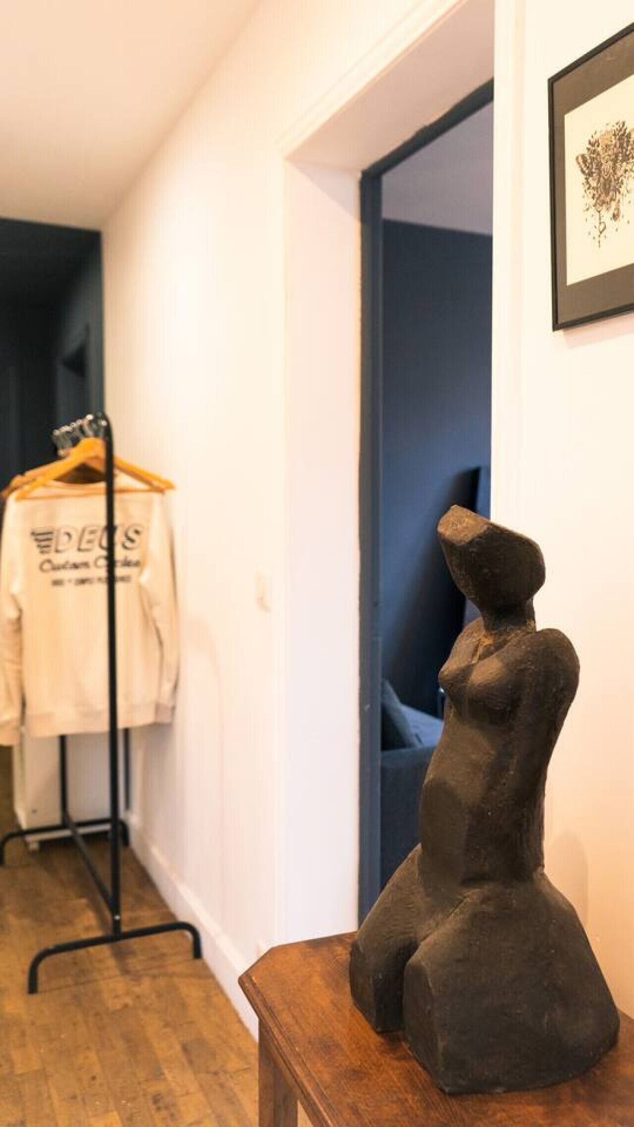 Un pasillo con un banco de madera, un perchero con una camisa blanca y una escultura en la pared.