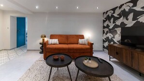 Ein modernes Wohnzimmer mit einer Couch, zwei Couchtischen, einem Fernseher und einer Wanddekoration.