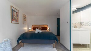 Ein Schlafzimmer mit Bett, Nachttisch, Wandregal und einem Badezimmer mit Waschbecken und Spiegel.