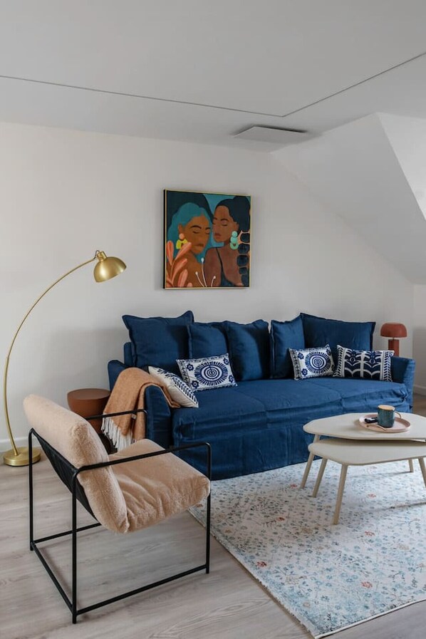 Una sala de estar moderna con un sofá azul, una silla de metal negro, una mesa de centro redonda y una lámpara de pie.