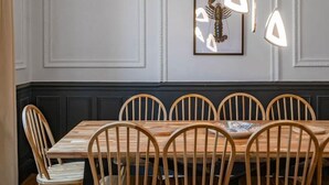 Une salle à manger avec une table et des chaises en bois, des murs blancs agrémentés de moulures décoratives et des luminaires suspendus.