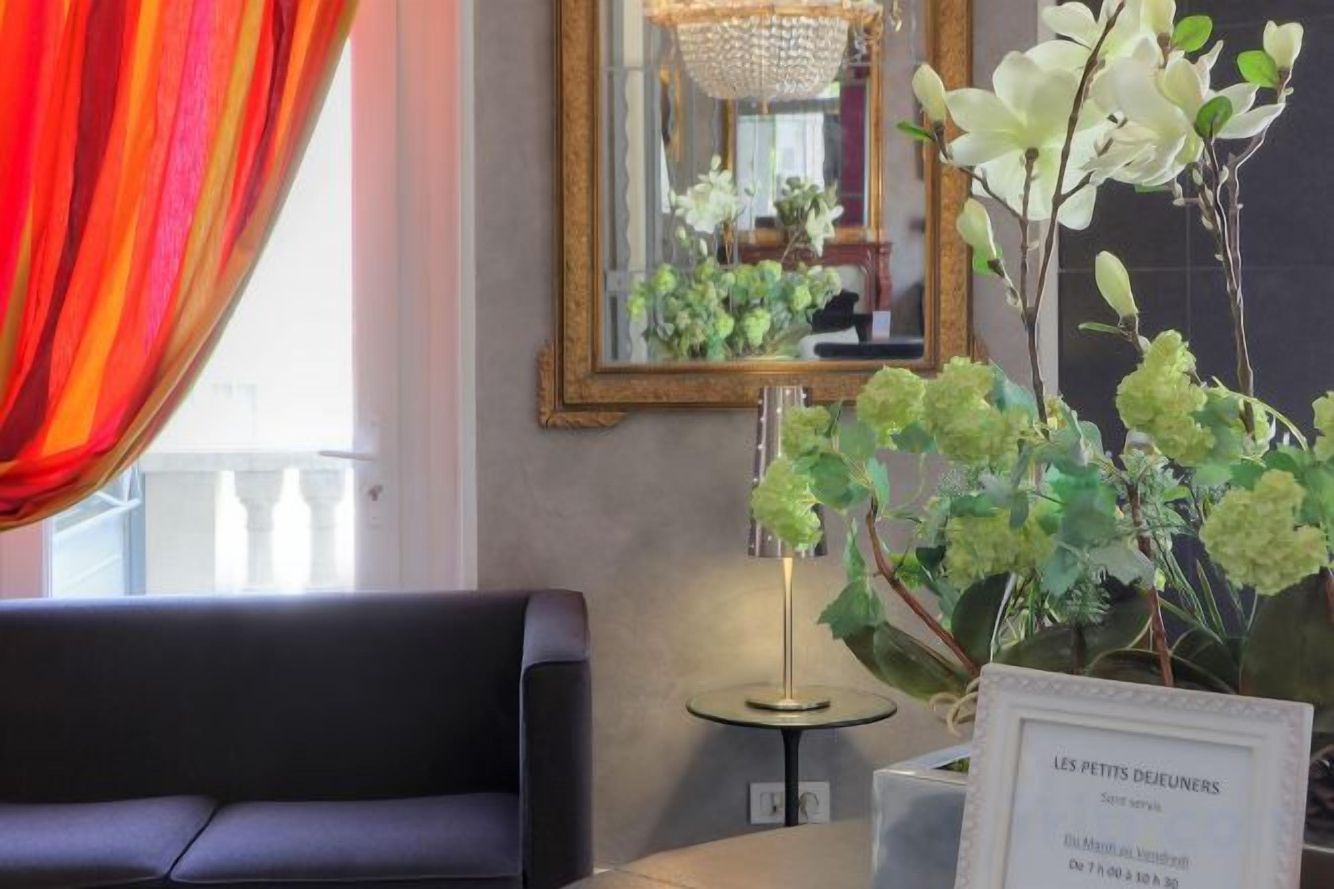 A hotel lobby with a sofa, a mirror, and a vase of flowers.