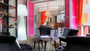 A lobby with black upholstered chairs, a round table with a book and a menu, and a large white lamp. - Best Western Hôtel Brittany la Baule Centre Et Plage (La Baule-Escoublac)