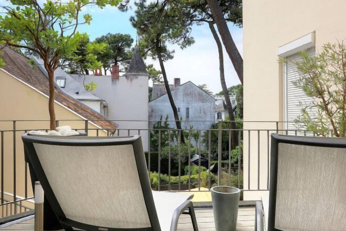 A balcony with two chairs and a table, overlooking a residential area with houses and trees.