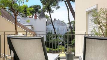 A balcony with two chairs and a table, overlooking a residential area with houses and trees.