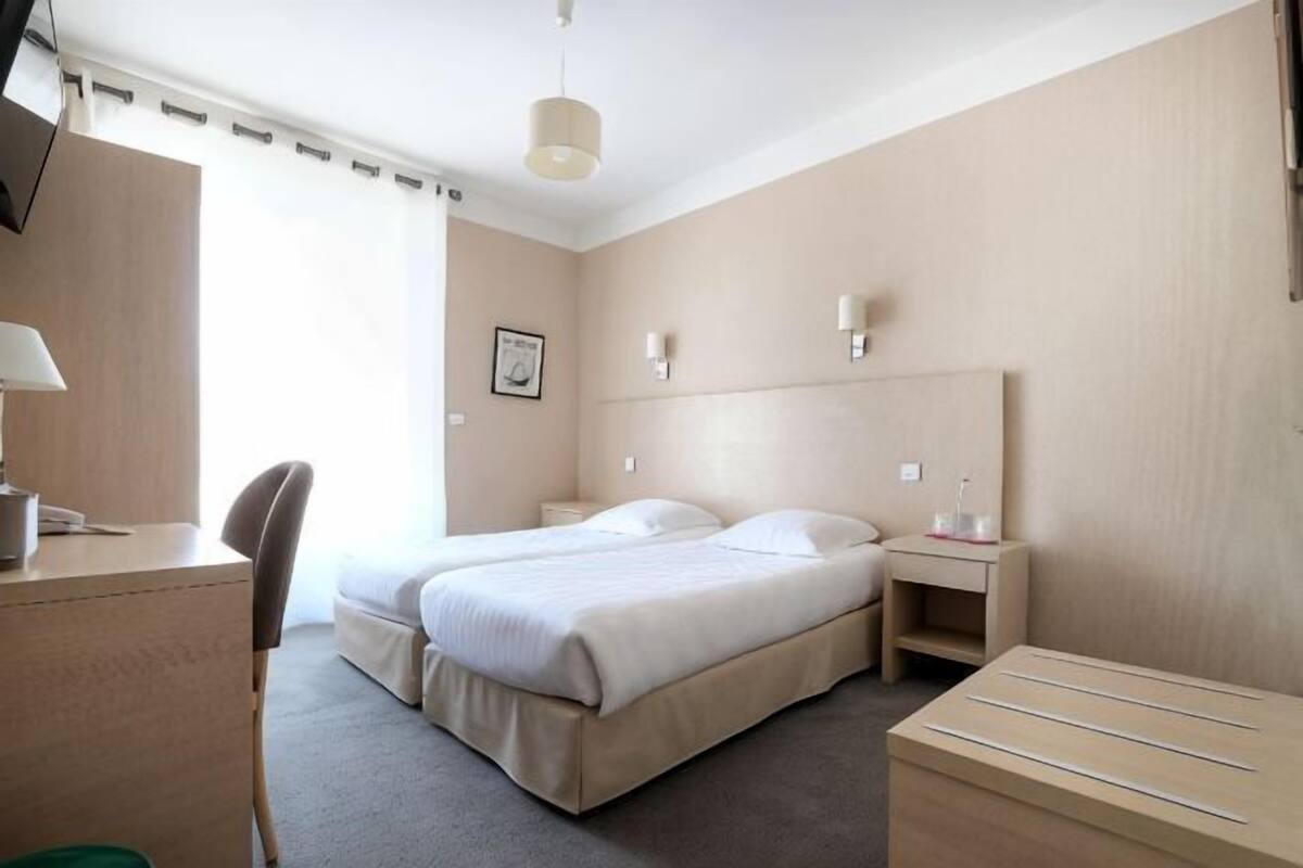 A hotel room with a bed, desk, chair, bedside table, and a small cabinet.