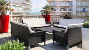 A balcony with wicker furniture and red planters, overlooking a coastal area with buildings. - Best Western Hôtel Brittany la Baule Centre Et Plage (La Baule-Escoublac)