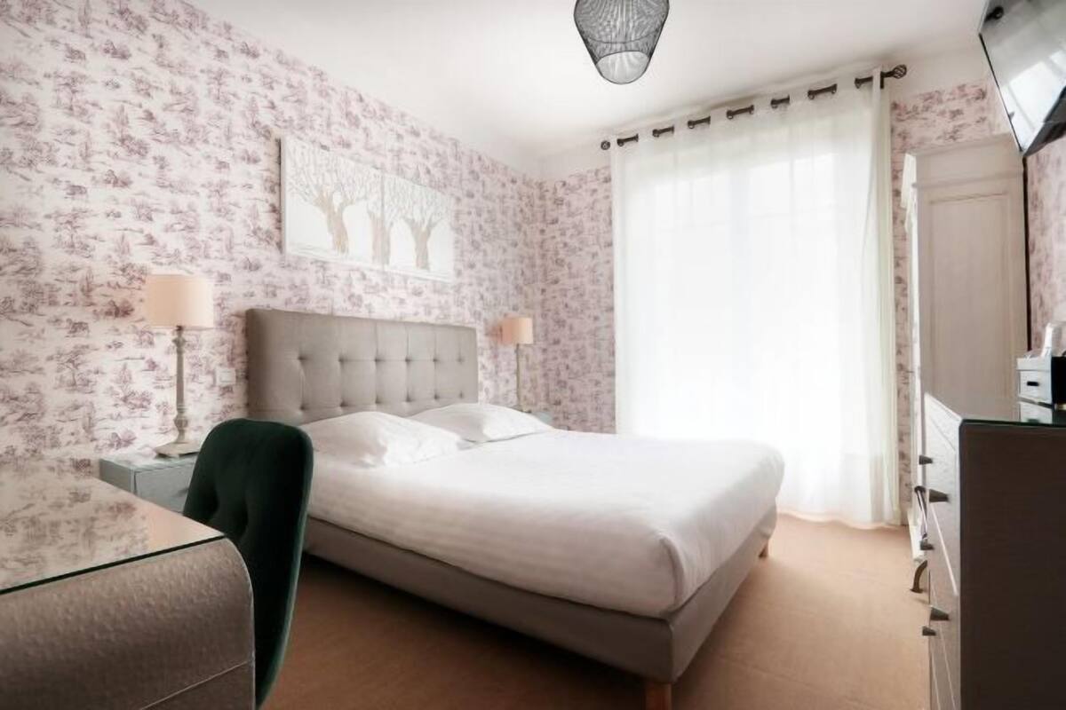 A bedroom with a bed, nightstands, a chair, a dresser, and a large window with curtains.