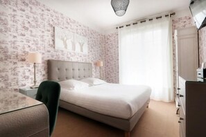 Ein Schlafzimmer mit Bett, Nachttischen, einem Sessel, einer Kommode und einem großen Fenster mit Vorhängen.