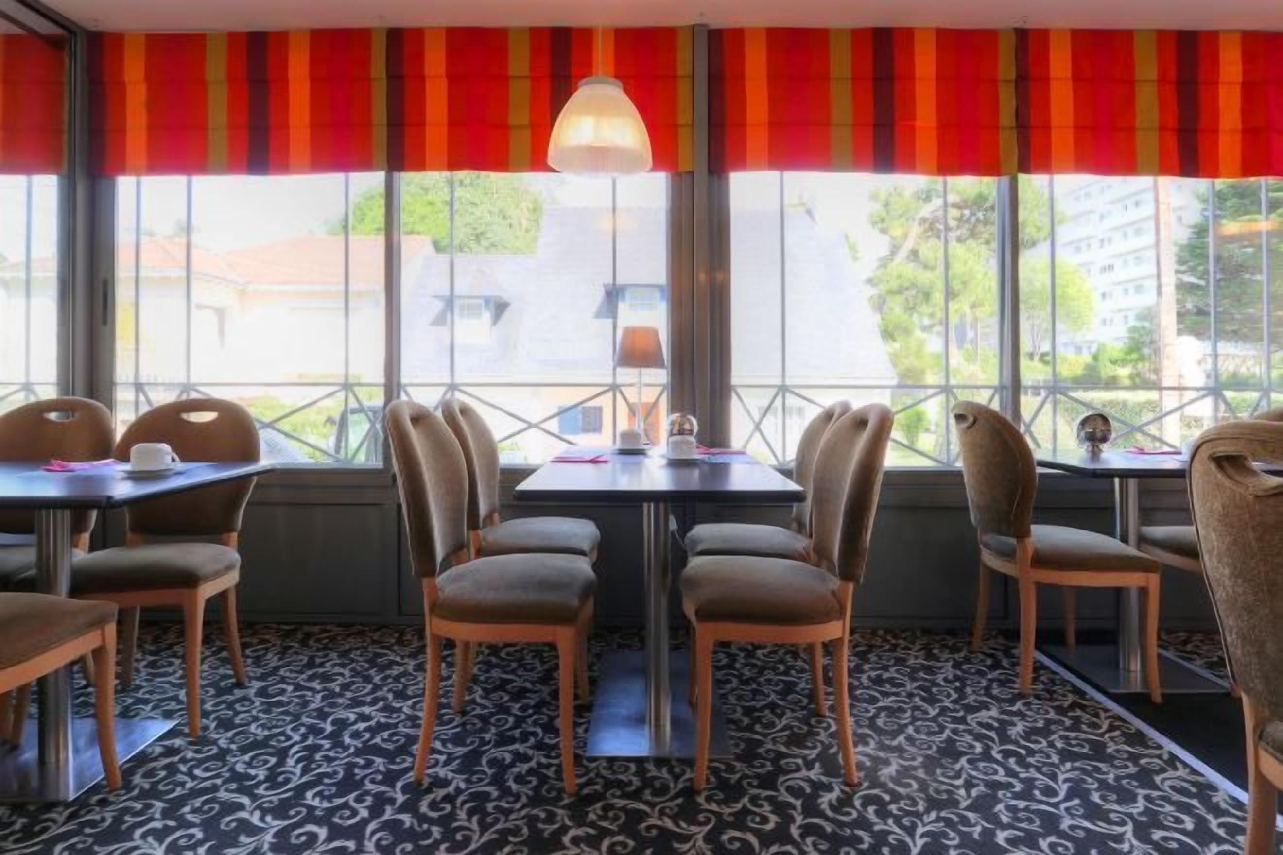 A restaurant with tables and chairs arranged for dining, large windows with a view, and a patterned carpet.