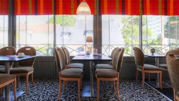 A restaurant with tables and chairs arranged for dining, large windows with a view, and a patterned carpet.