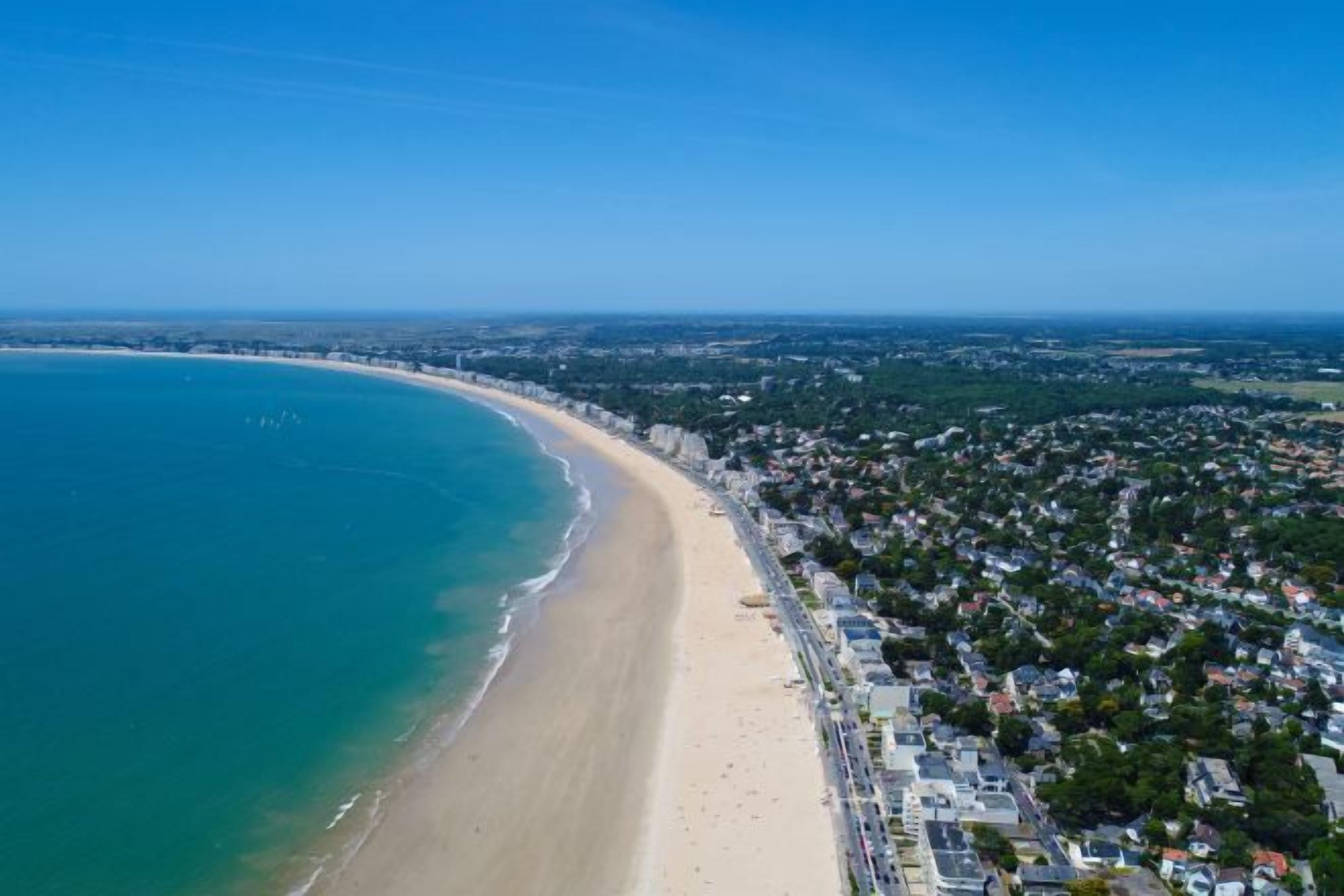 Vista aérea de una ciudad costera con playa, zonas residenciales y cielo despejado.