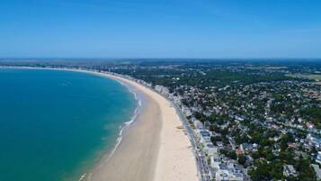 Vista aérea de una ciudad costera con playa, zonas residenciales y cielo despejado.
