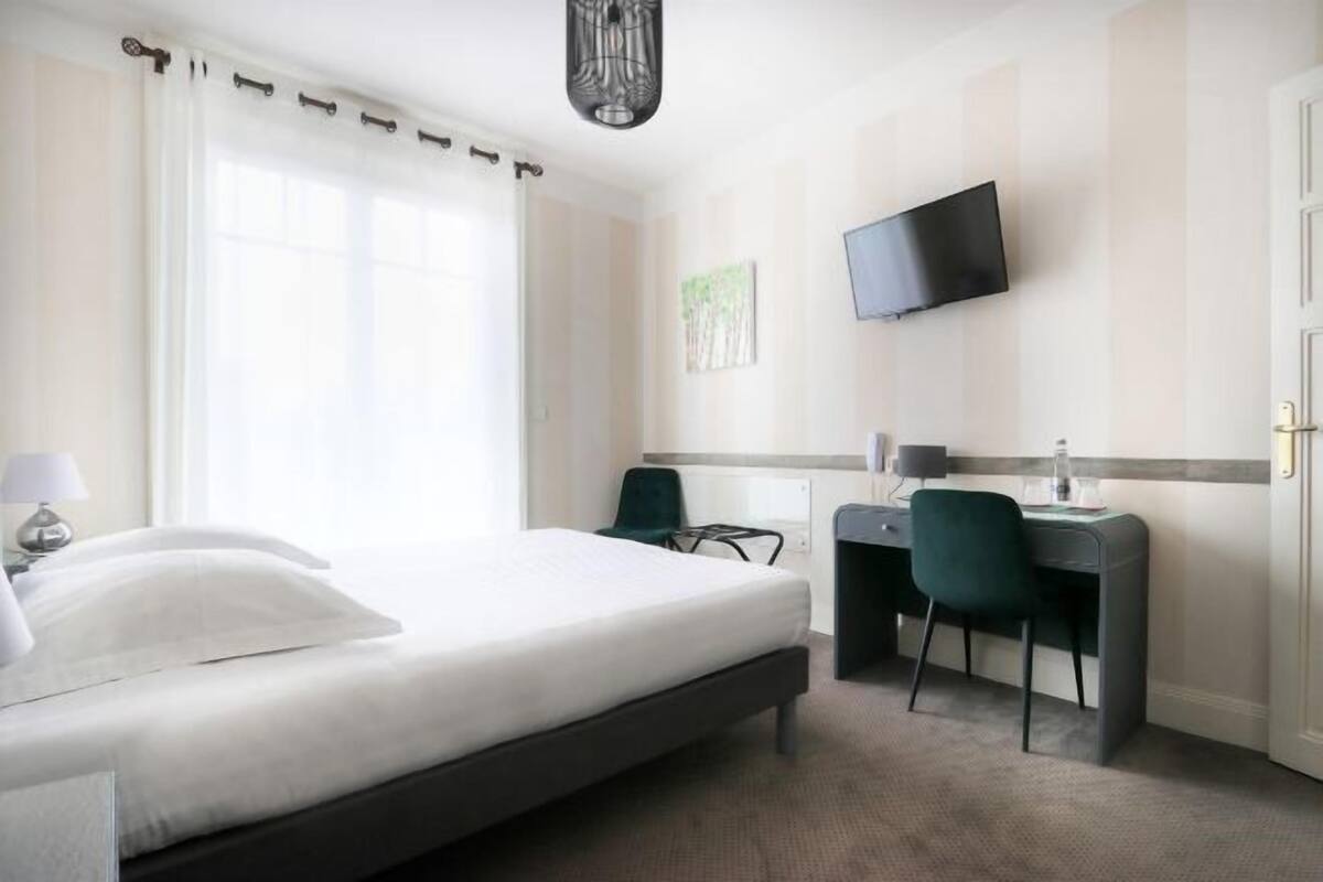 A hotel room with a bed, desk, chair, TV, and artwork on the wall.
