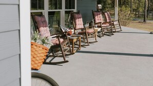 Une rangée de fauteuils à bascule avec des coussins à carreaux sur une terrasse en béton, avec une maison et des arbres en arrière-plan.