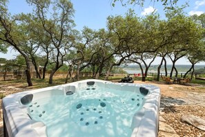 Relax in a serene outdoor setting with a hot tub surrounded by lush greenery and a tranquil body of water.