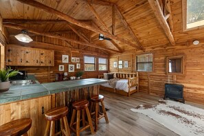Cozy cabin-style interior with a high ceiling, central island kitchen, and a fireplace.