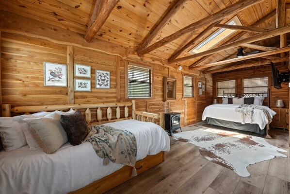 Cozy retreat with a large bed, a smaller bed, and a wooden bench, set amidst framed pictures and exposed wooden beams.