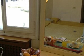 A hotel room with a bed, a window, a mirror reflecting the room, and a table with a bowl of fruit. - Hotel Airone (Venice)
