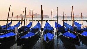 A row of gondolas docked at a pier with a cityscape in the background. - Hotel Airone (Venice)