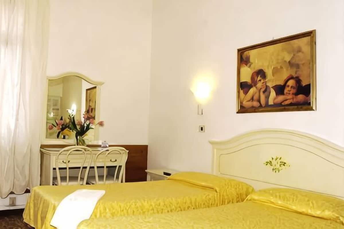 Una habitación de hotel con una cama, un escritorio con espejo y un cuadro en la pared.