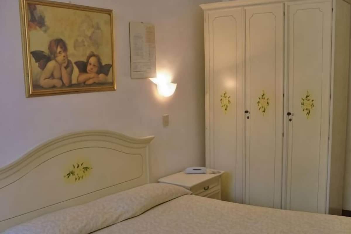 Un dormitorio con cama, mesita de noche, armario y luz empotrada en la pared.