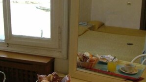 A hotel room with a bed, a window, a mirror reflecting the bed, a tray with breakfast items, and a bowl of fruit. - Hotel Airone (Venice)
