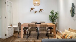 Un coin repas avec une table en bois et des chaises en osier, un luminaire suspendu et un cactus accroché au mur.