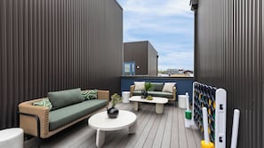 A rooftop patio with a sofa, two small tables, and a seating area with cushions.