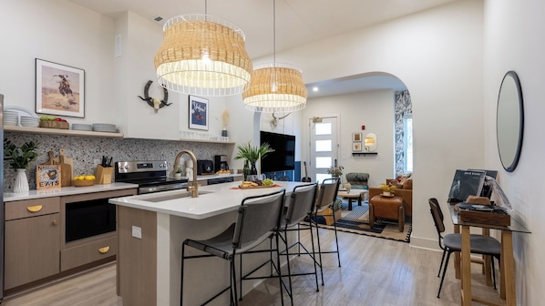 A modern kitchen with a central island, pendant lights, and a dining area with chairs and a table.