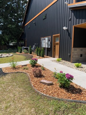 Il s’agit d’un bâtiment moderne à l’extérieur sombre, doté d’une porte en bois et d’un garage. On y trouve des boîtiers électriques à l’extérieur et un chemin menant à l’entrée.