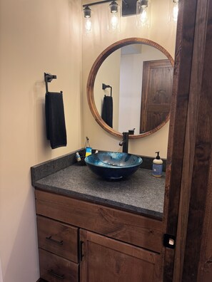 A bathroom with a wooden vanity, a round mirror, and a blue vessel sink. - Charming and Cozy Retreat in Newaygo, MI- The Rustic Barn dominium (Newaygo)