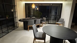 A modern dining area with a round table and chairs, a black bookshelf, and a large window with a view of the outdoors. - Prime Soul Brooklin (Sao Paulo)