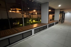 A modern indoor space with a long bench, glass walls, and a tiled floor. - Prime Soul Brooklin (Sao Paulo)