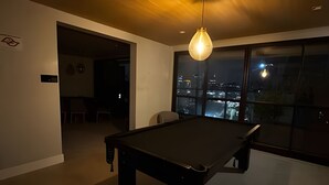 A modern room with a pool table, a hanging light fixture, and a large window offering a city view. - Prime Soul Brooklin (Sao Paulo)