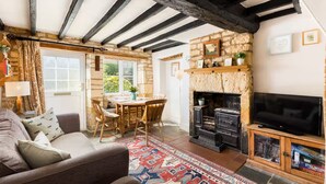 Una sala de estar acogedora con vigas de madera a la vista, una chimenea de piedra, un televisor y un comedor con mesa y sillas.