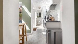 A modern kitchen with a central island, a dining area with a wooden table and chairs, and a view of a garden through a glass door. - Pass the Keys | Stunning 3-bed Retreat in the Heart of York (York)