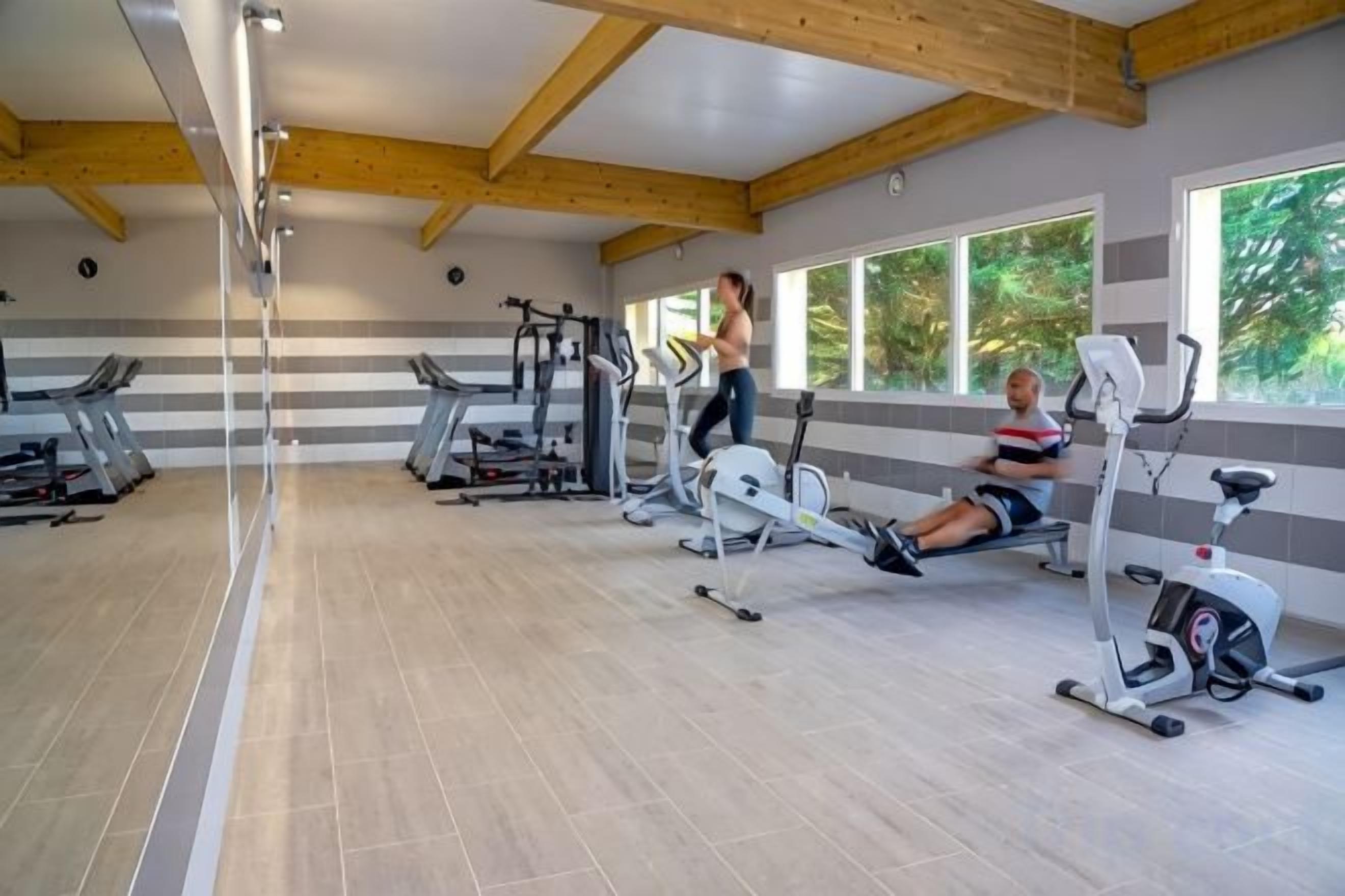 A gym with exercise equipment, large windows, and a wooden ceiling.
