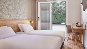 A hotel room with two beds, a desk, a chair, and a large window with a view of greenery. - Kyriad Sens (Sens)